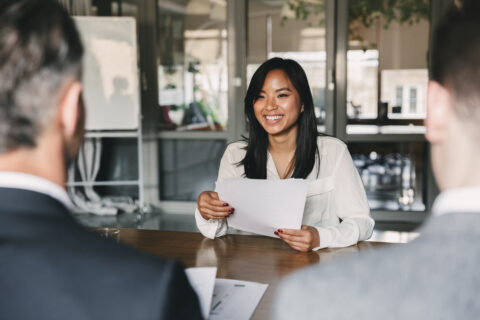 A young woman holding her resume speaking to two businessman at an interview.